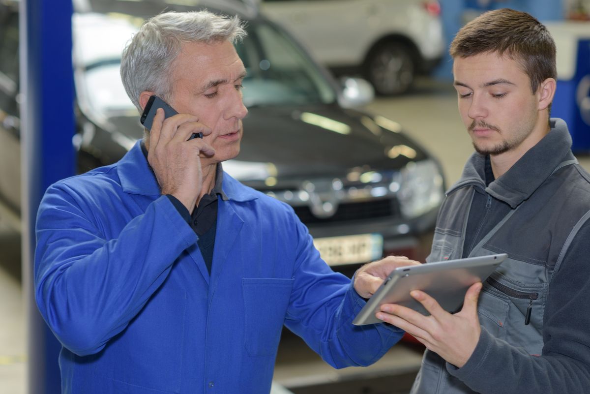 Garage owner on the phone while an apprentice checks a tablet